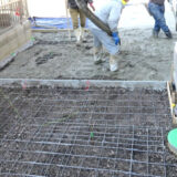 Concrete pouring process at a residential construction site. Professional workers spreading fresh concrete over wire mesh reinforcement.