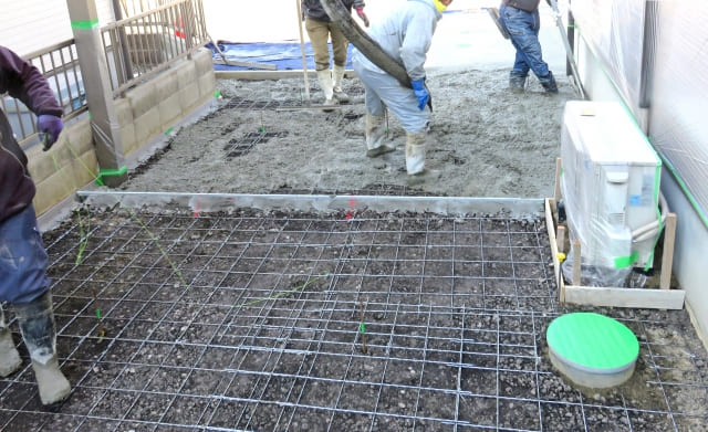 Concrete pouring process at a residential construction site. Professional workers spreading fresh concrete over wire mesh reinforcement.