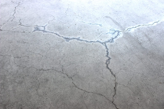 経年劣化や乾燥収縮により大きなひび割れ（クラック）が発生したコンクリート床の表面。ハツリ作業や補修が必要な状態。