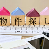 Wooden house blocks with the Japanese text "物件探し" (Property Search) placed on a computer keyboard.