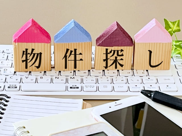 Wooden house blocks with the Japanese text "物件探し" (Property Search) placed on a computer keyboard.