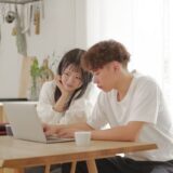 A 30s couple looking at a laptop together at home, searching for ideal homes and discussing their financial planning online.