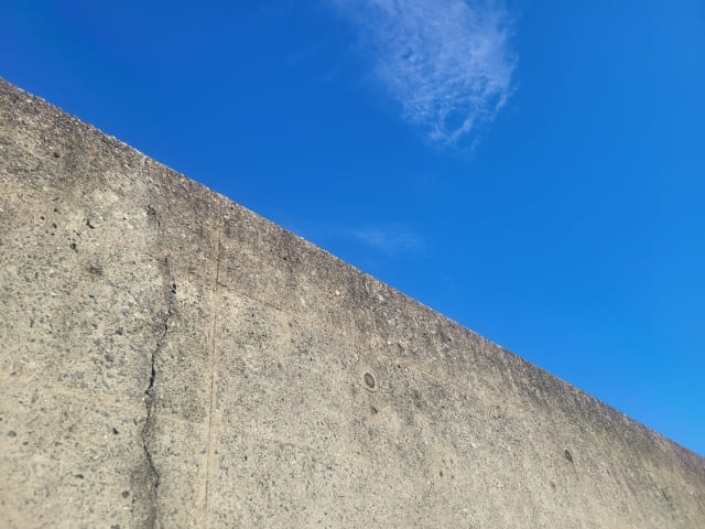 青空を背景にしたコンクリート擁壁のローアングル写真。高くそびえるコンクリート構造物が、確かな施工と技術力を象徴。