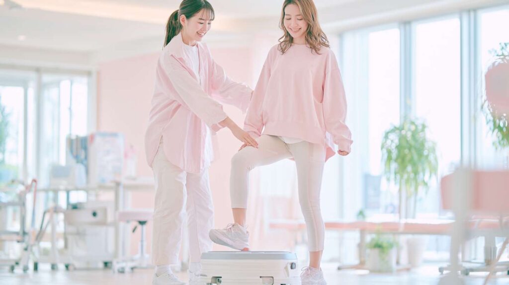 整骨院でスタッフのサポートを受けながらバランストレーニングを行う女性