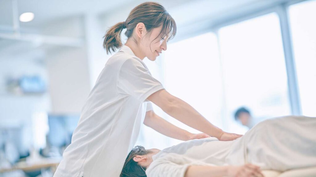 整骨院の施術室で、施術者が患者の背中に手技療法を行っている様子