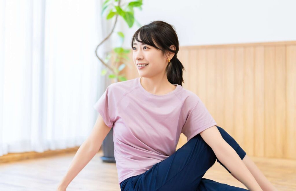 自宅の床でウエストをひねるストレッチをしながら微笑む女性