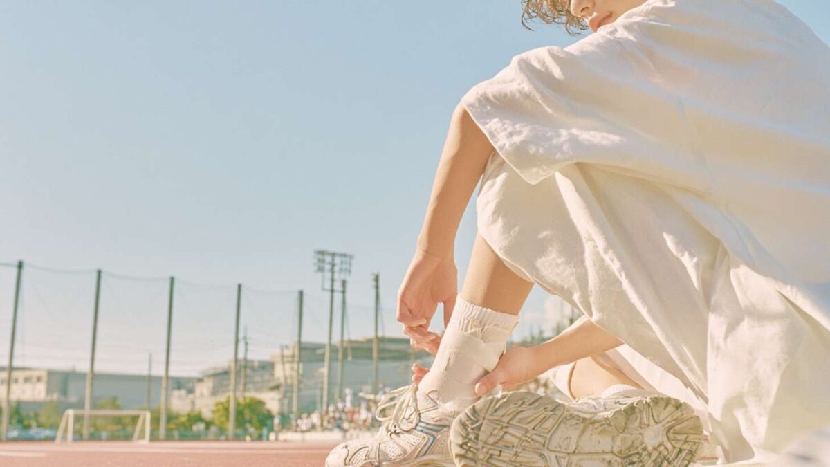 A woman sitting on an outdoor running track adjusting an ankle support brace