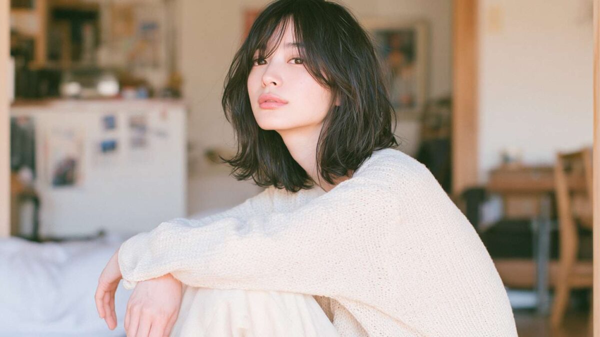 A woman sitting indoors with her arms resting on her knees, wearing a knit sweater