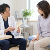 Orthopedic doctor explaining hip pain using an anatomical hip joint model during a consultation with a female patient.